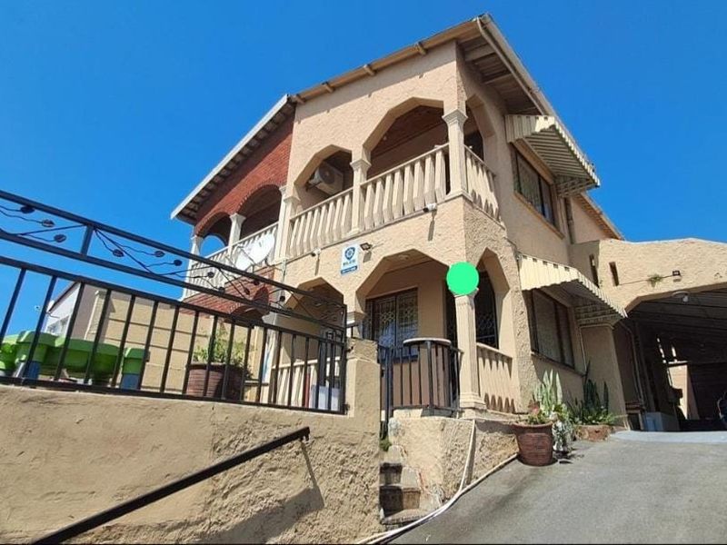 Front elevation of a multi-story house featuring a balcony, covered carport, and external staircase with security fencing.