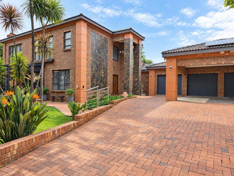 A well-maintained double-story brick residence featuring a spacious paved driveway, triple garage, and attractive slate-clad architectural accents.