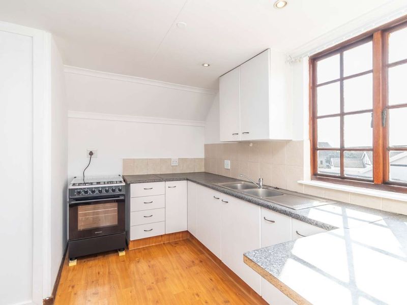A functional kitchen featuring white cabinetry, laminate countertops, a stainless steel double sink, and timber-framed windows, offering a clean and practical workspace.
