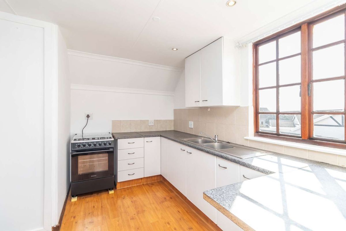 A functional kitchen featuring white cabinetry, laminate countertops, a stainless steel double sink, and timber-framed windows, offering a clean and practical workspace.