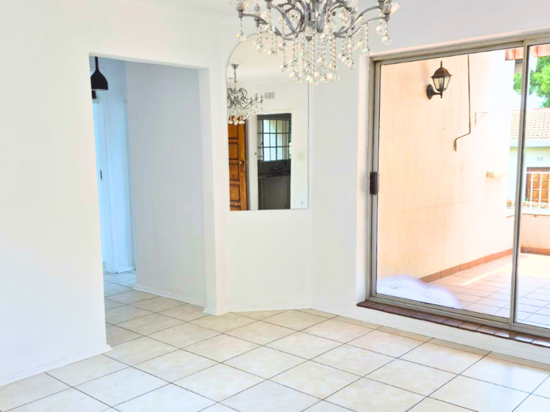 Bright and spacious living area featuring neutral tiled flooring, a large sliding glass door leading to a patio, and a decorative ceiling chandelier.
