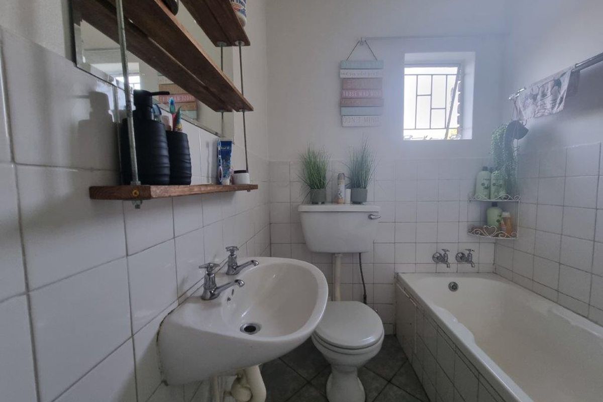 A functional bathroom featuring a white pedestal basin, a standard toilet, and a bathtub with wall-mounted taps and tiled splashbacks.