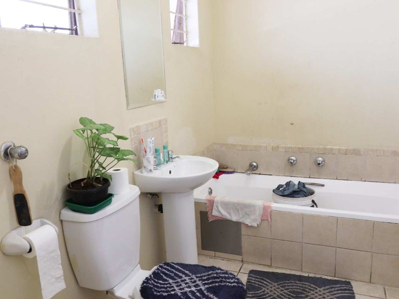 A functional bathroom featuring a pedestal basin, built-in bathtub with tiled surround, and wall-mounted mirror, requiring cosmetic updates to improve its overall condition.