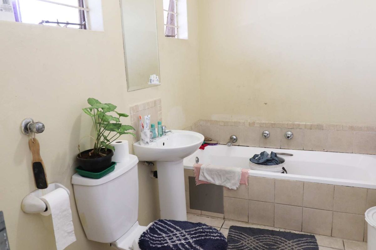 A functional bathroom featuring a pedestal basin, built-in bathtub with tiled surround, and wall-mounted mirror, requiring cosmetic updates to improve its overall condition.