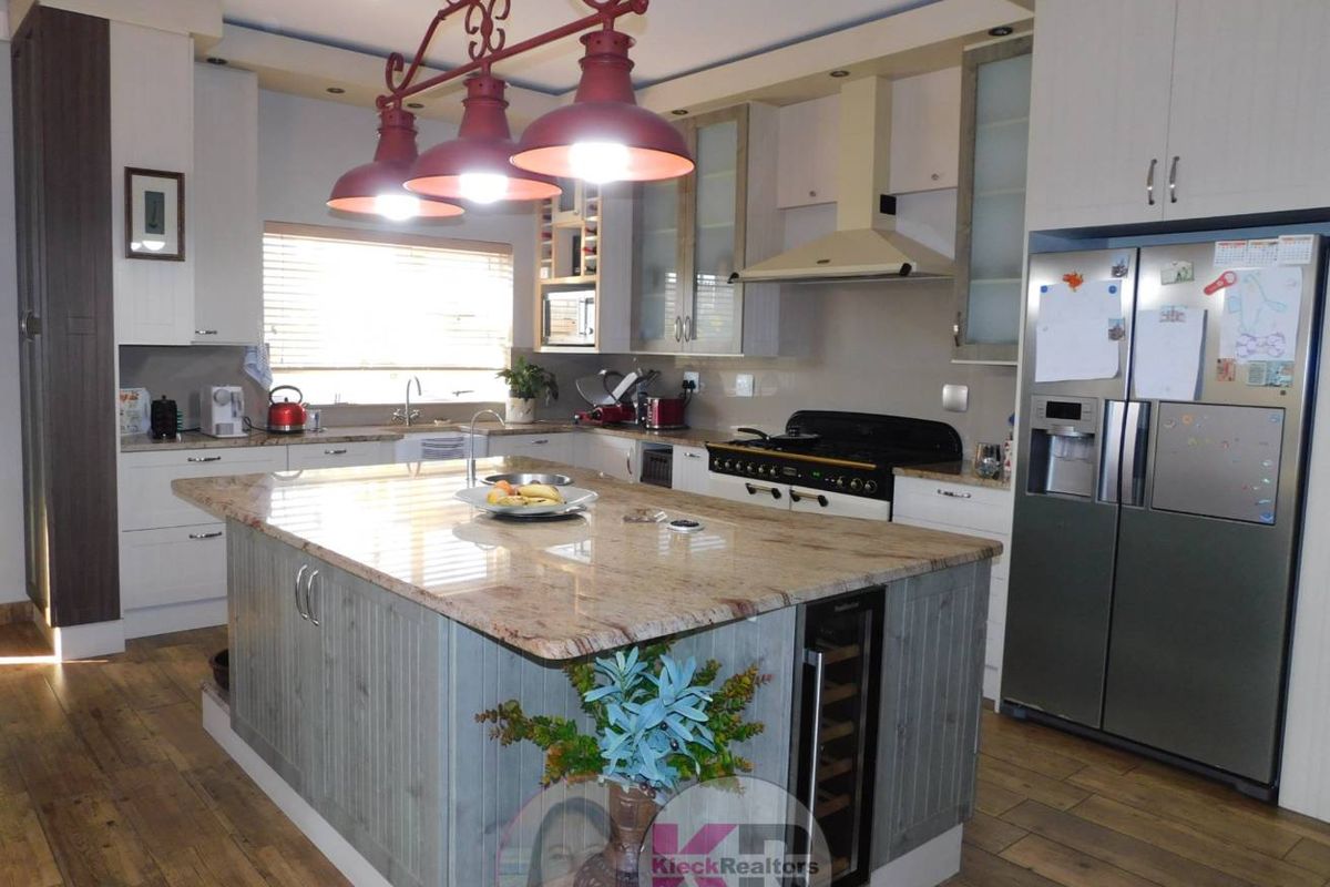 Modern kitchen featuring a large central island with granite countertops, built-in cabinetry, integrated wine cooler, and a gas stove with extractor fan.