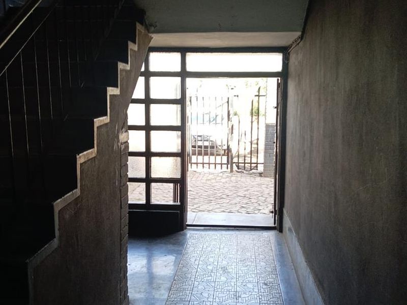 A dimly lit apartment entrance hallway featuring a staircase, tiled flooring, and a glass-paneled door leading to the exterior.