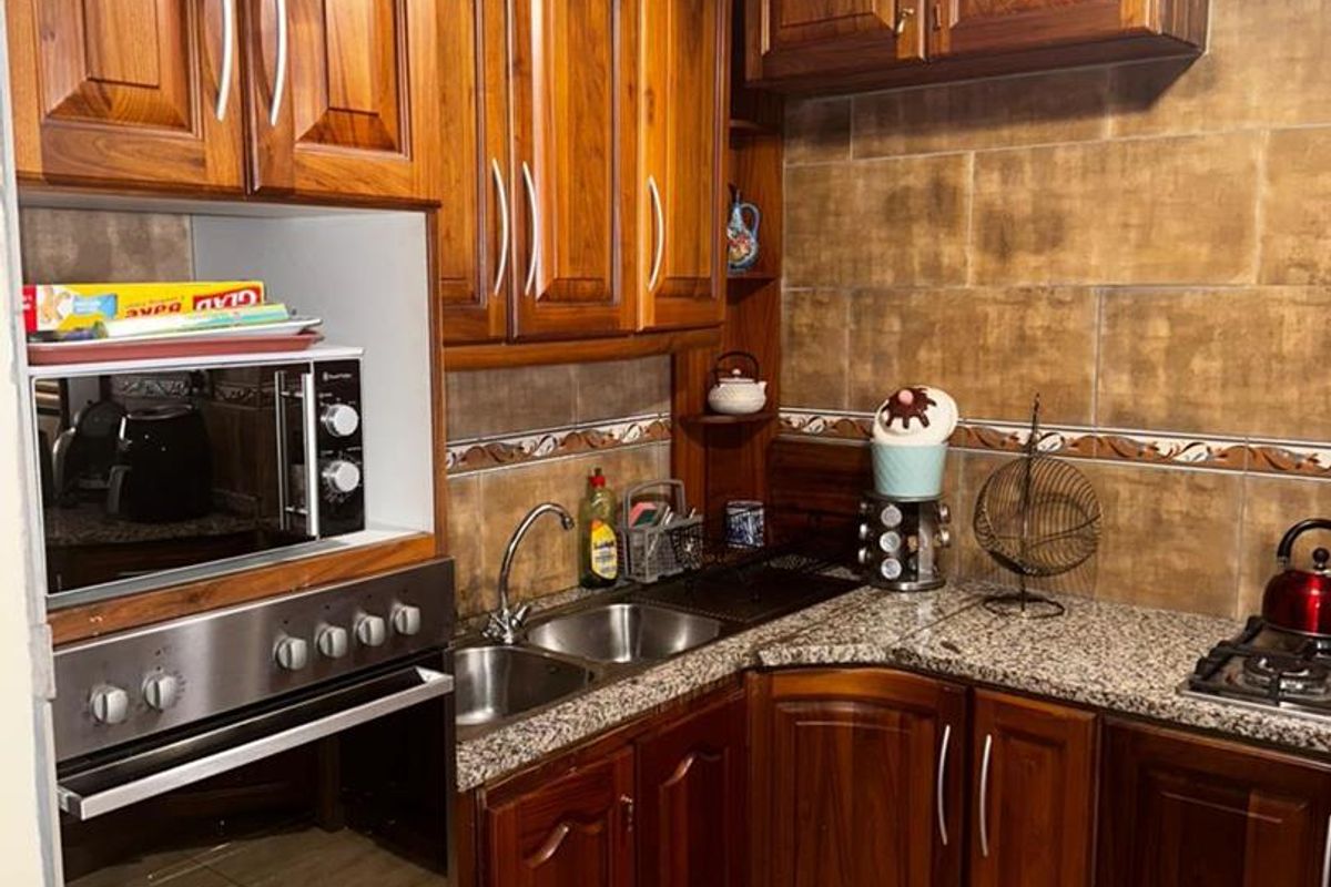 Compact kitchen featuring traditional timber cabinetry, granite countertops, integrated oven, and tiled splashback.