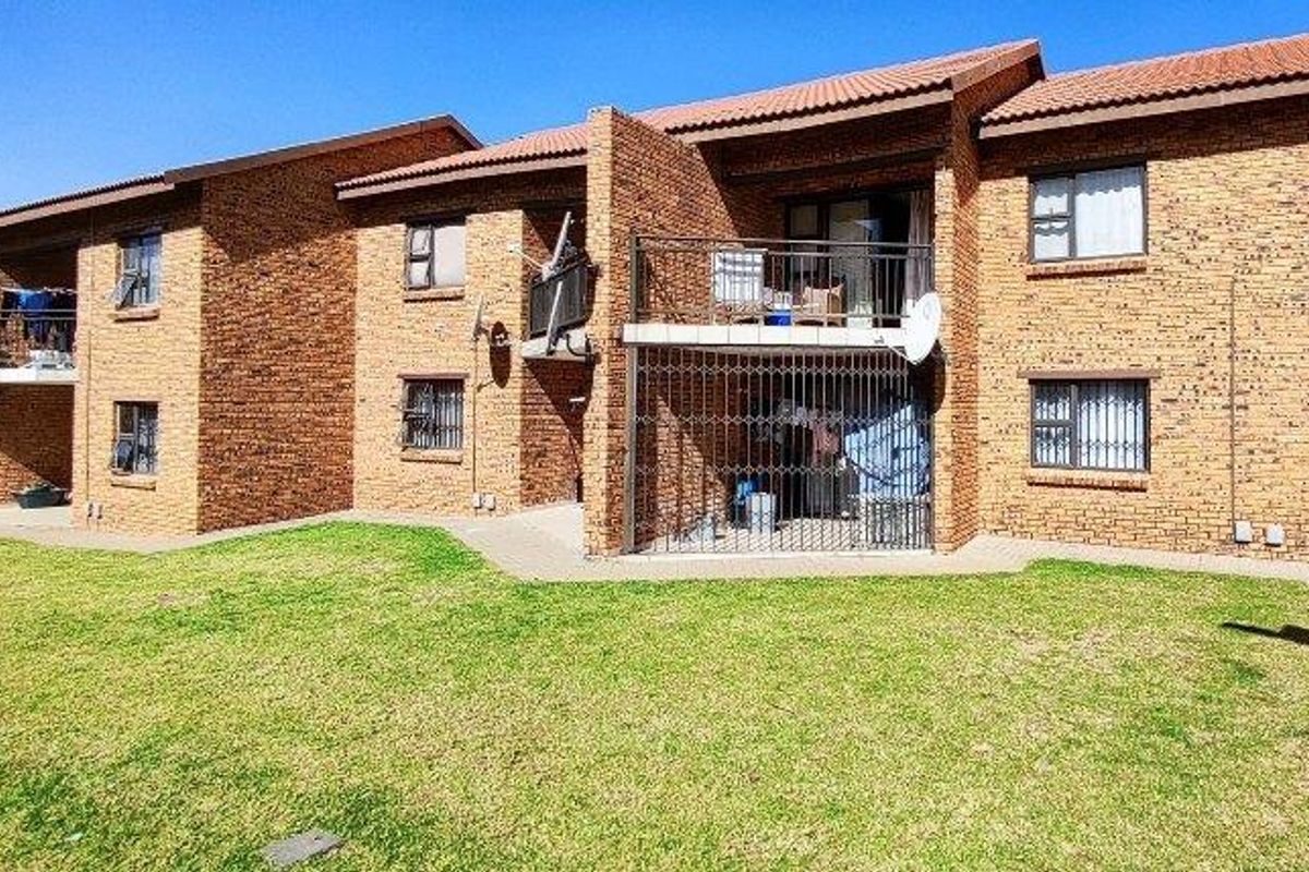 Rear view of a multi-story townhouse complex featuring face-brick facade, tiled roofing, private balconies, and ground-floor security gates overlooking a communal lawn area.