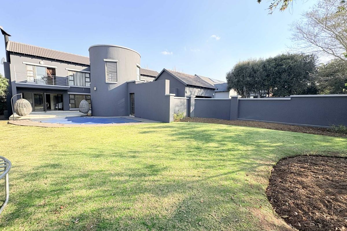Rear view of a modern two-story house featuring a swimming pool, landscaped lawn, and a secure boundary wall.