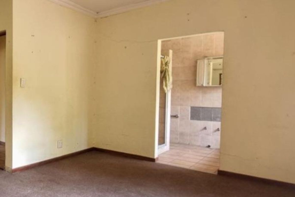 An empty living area featuring neutral walls and carpeting, with an open doorway leading into an adjacent tiled bathroom space.
