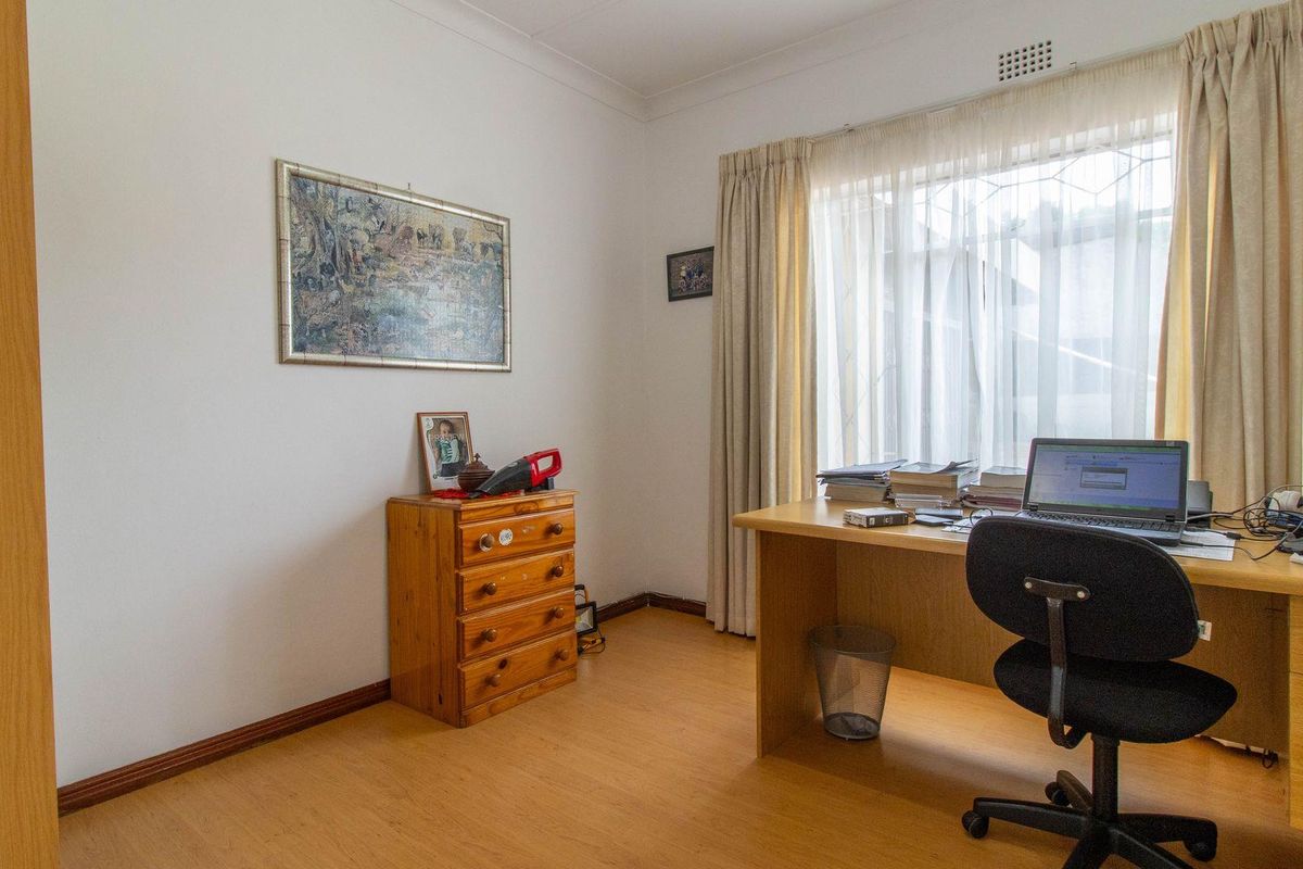 A functional bedroom or home office space featuring laminate flooring, a large window with curtains, and neutral wall finishes.