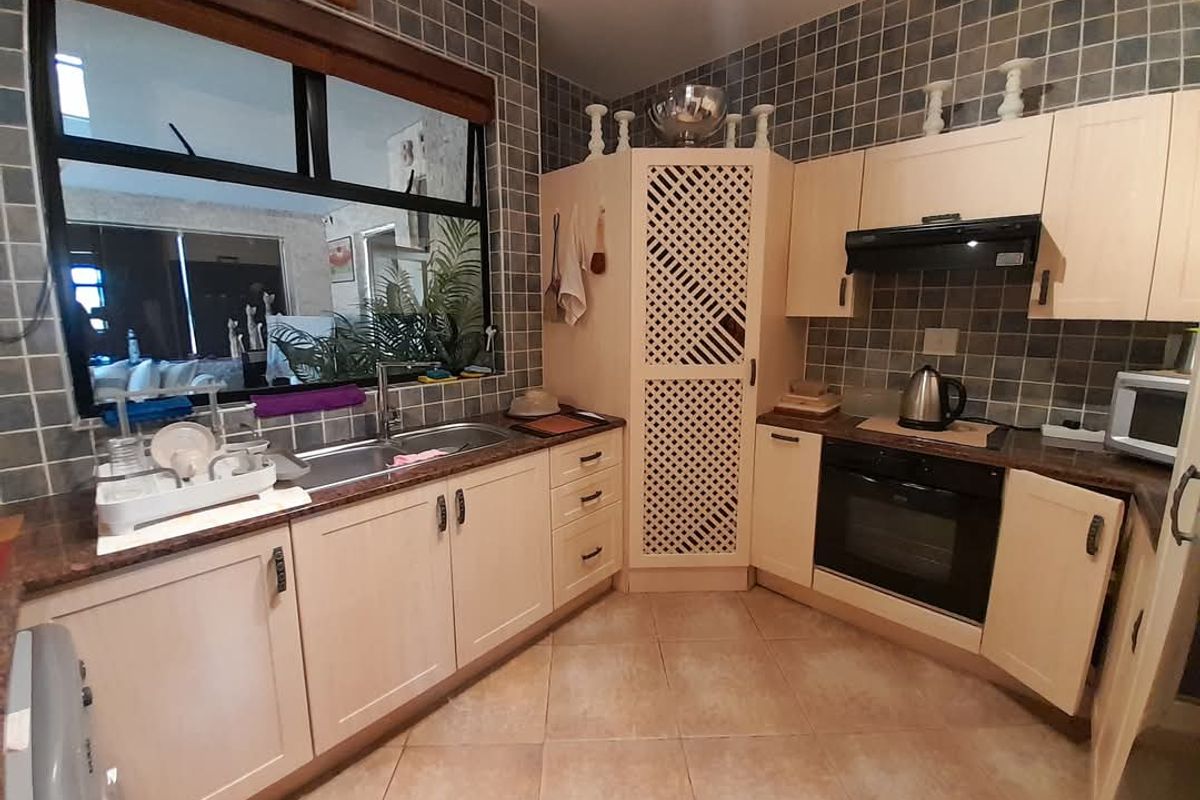 A functional kitchen featuring light-toned cabinetry, granite countertops, a built-in oven, extractor fan, and a double-basin sink with a window overlooking the living area.