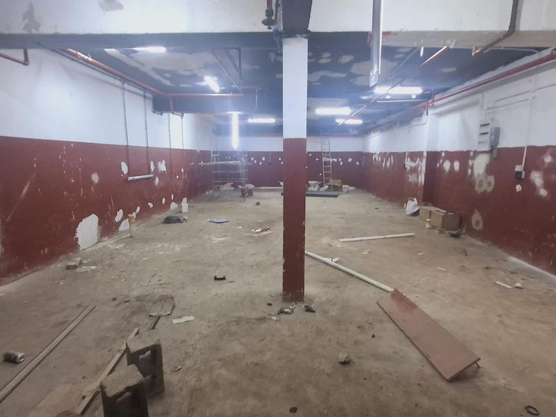 An expansive, unfinished industrial utility space featuring exposed piping, concrete flooring, and structural columns, currently in a shell condition requiring renovation.