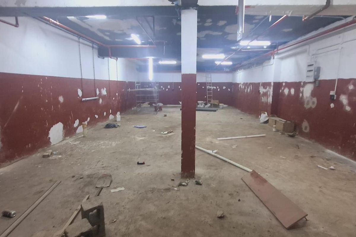 An expansive, unfinished industrial utility space featuring exposed piping, concrete flooring, and structural columns, currently in a shell condition requiring renovation.