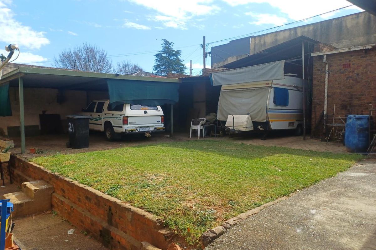 Rear yard featuring a raised lawn area, brick retaining wall, and covered parking or storage structures.