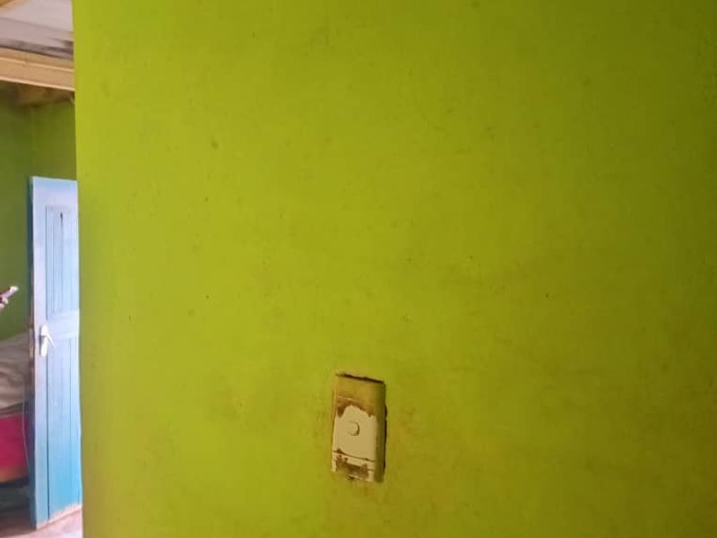 A close-up view of a lime green wall featuring a damaged light switch cover, showing signs of wear and maintenance needs.