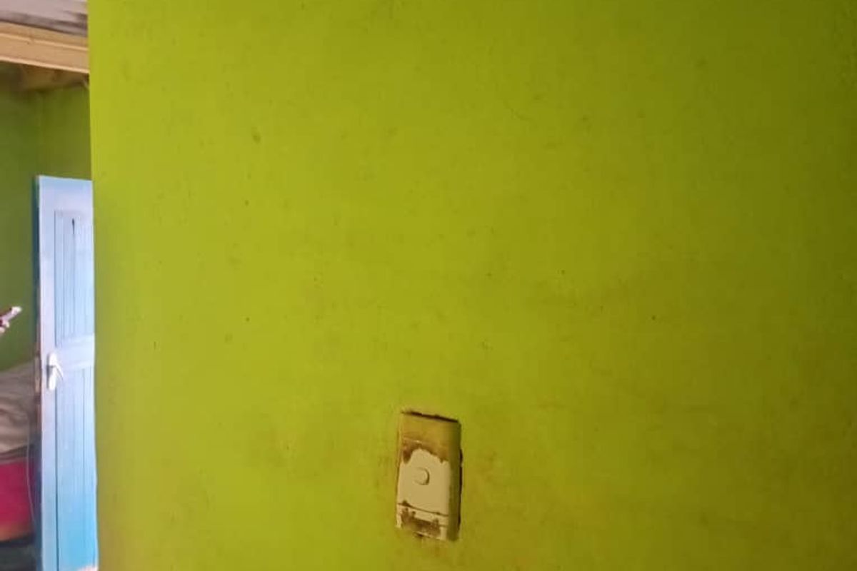 A close-up view of a lime green wall featuring a damaged light switch cover, showing signs of wear and maintenance needs.