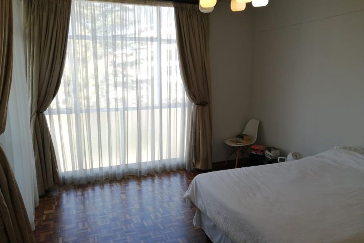 A bedroom featuring parquet flooring and a large floor-to-ceiling window that allows for ample natural light.