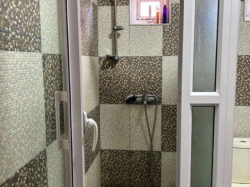 A functional bathroom featuring a shower enclosure with tiled walls, a toilet, and a small window for ventilation.