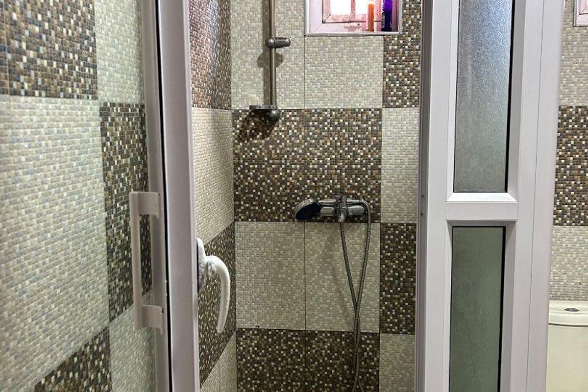 A functional bathroom featuring a shower enclosure with tiled walls, a toilet, and a small window for ventilation.