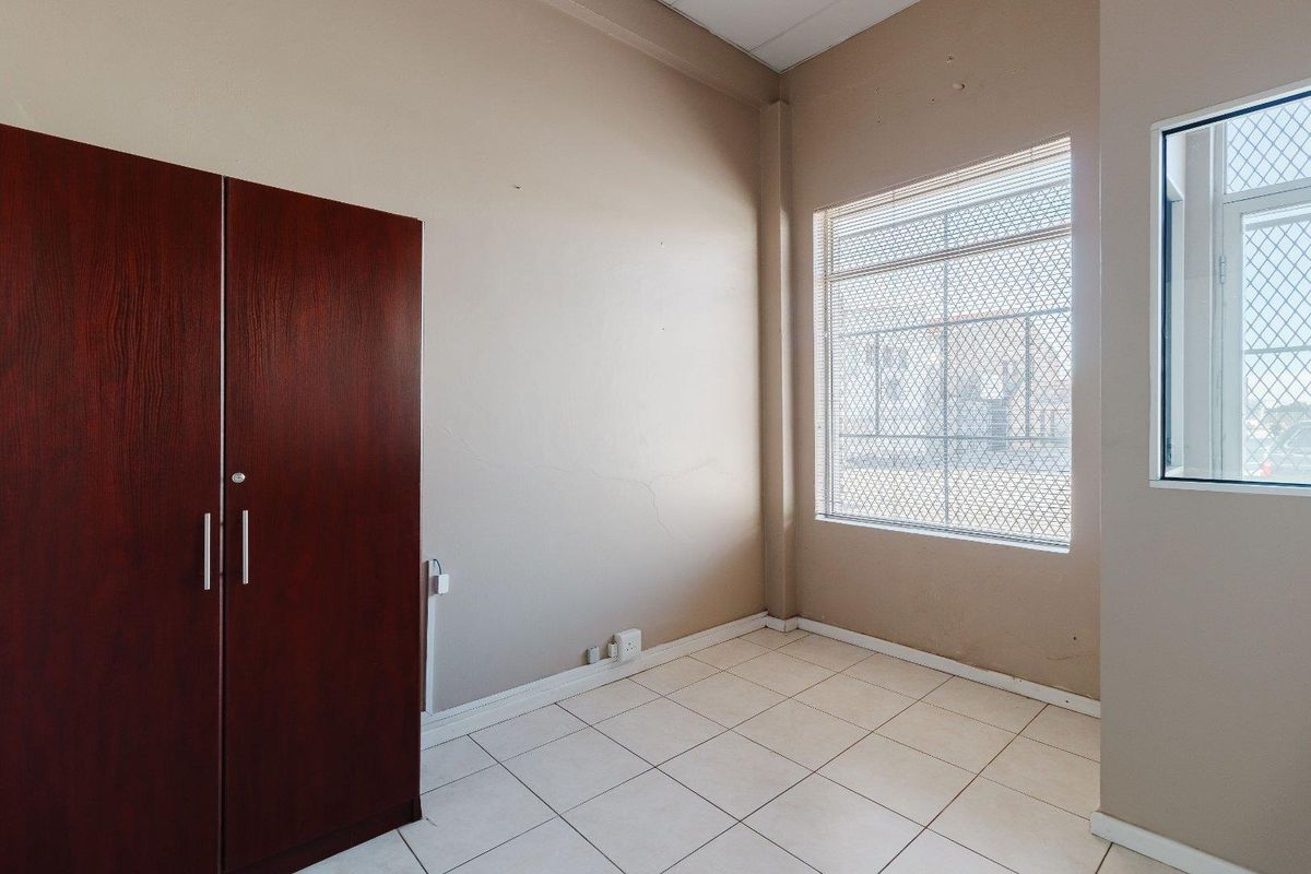 A compact office space featuring tiled flooring, a built-in cupboard, and a window fitted with security mesh.