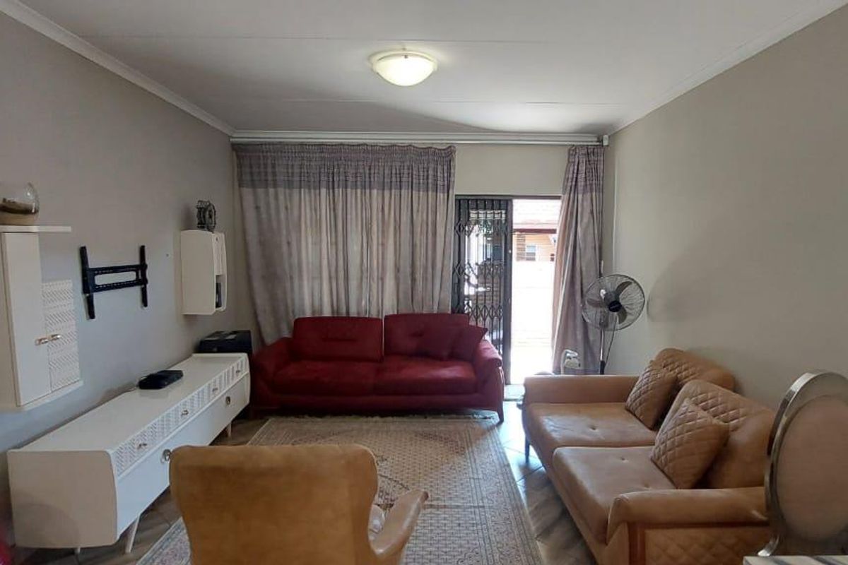 A living room featuring tiled flooring, neutral wall finishes, and a sliding door with security gate leading to the exterior.