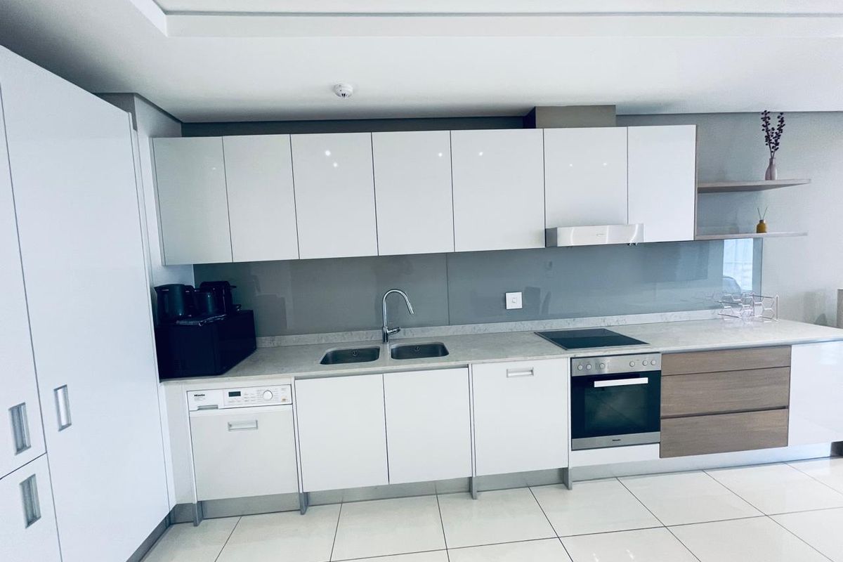 Modern kitchen featuring sleek white cabinetry, integrated appliances, stone countertops, glass splashback, and high-quality tiled flooring in a clean, contemporary design.