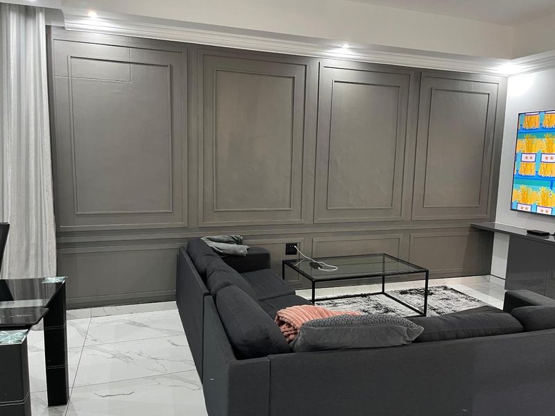 A modern living room featuring elegant grey wainscoting, polished marble-look tiled flooring, and recessed ceiling lighting.