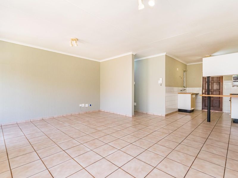 Spacious open-plan living area featuring tiled flooring, neutral walls, and a functional kitchen layout with a breakfast bar.