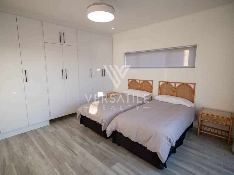 A modern bedroom featuring extensive built-in cupboards, light-toned laminate flooring, and a sleek horizontal window providing natural light.