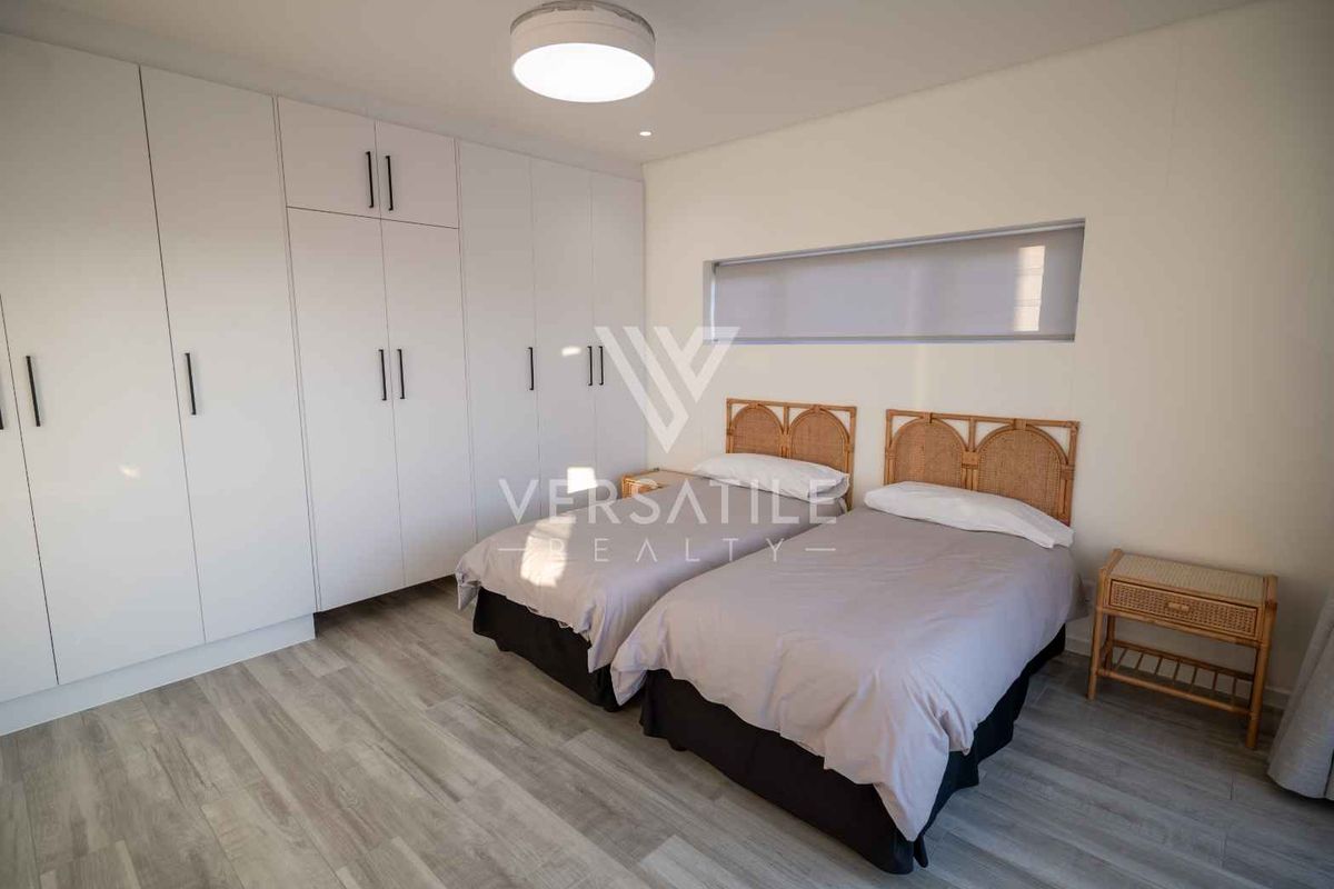 A modern bedroom featuring extensive built-in cupboards, light-toned laminate flooring, and a sleek horizontal window providing natural light.