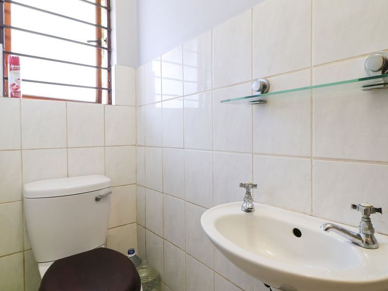 A functional bathroom featuring a wall-mounted basin, toilet, and tiled walls. The space is clean and ready for potential cosmetic updates.