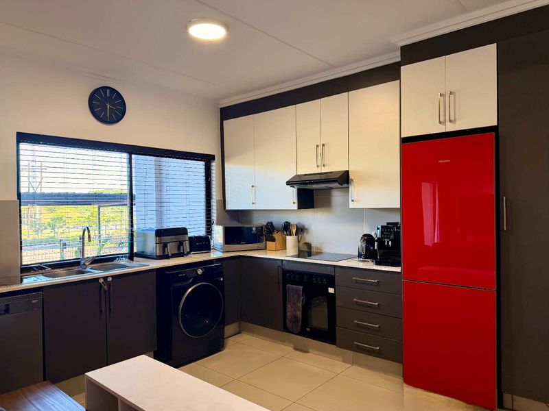 Modern kitchen featuring two-tone cabinetry, integrated appliances, stainless steel sink, and tiled flooring with ample natural light from the large window.