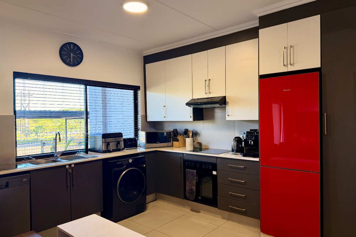 Modern kitchen featuring two-tone cabinetry, integrated appliances, stainless steel sink, and tiled flooring with ample natural light from the large window.