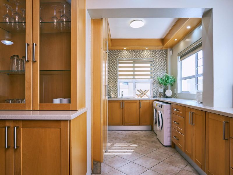 A functional laundry room featuring light wood cabinetry, stone-look countertops, mosaic tile backsplash, and integrated laundry appliance space.