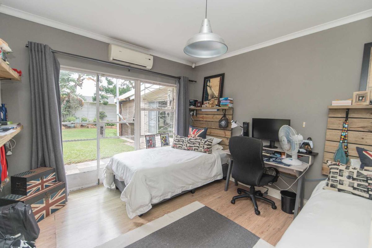 A functional bedroom featuring wood-look flooring, a wall-mounted air conditioning unit, and sliding glass doors providing direct access to the rear garden.