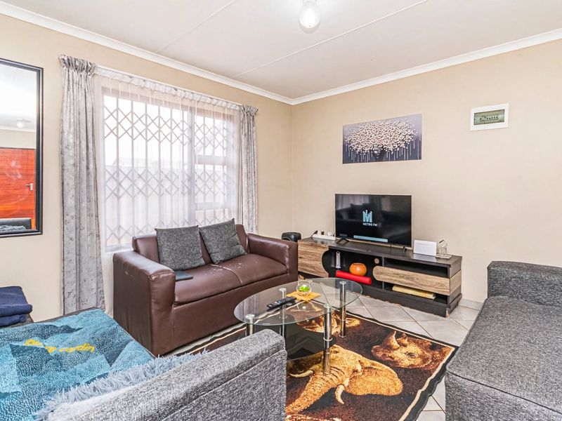 A comfortable living room featuring tiled flooring, neutral wall finishes, and a large window fitted with a security gate.