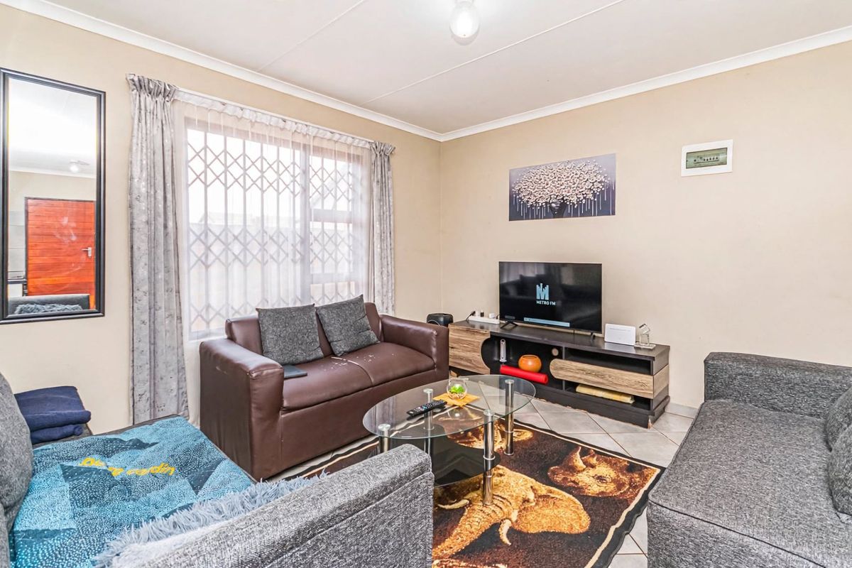 A comfortable living room featuring tiled flooring, neutral wall finishes, and a large window fitted with a security gate.