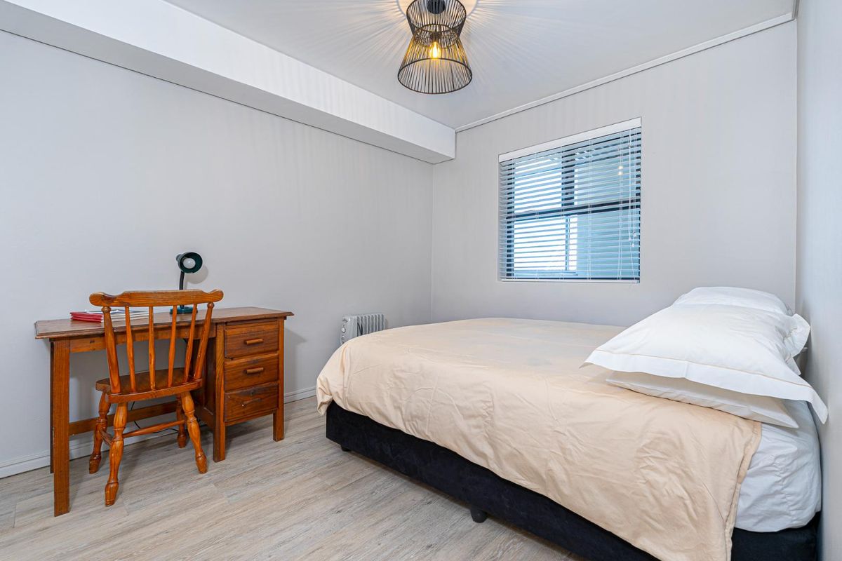 A well-maintained bedroom featuring light wood-look flooring, neutral wall tones, and a window fitted with horizontal blinds.