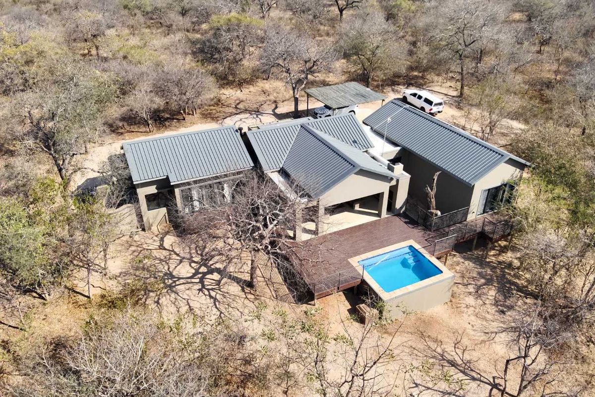 Aerial view of a modern bushveld home featuring a metal roof, timber decking, and a private swimming pool set in a natural landscape.