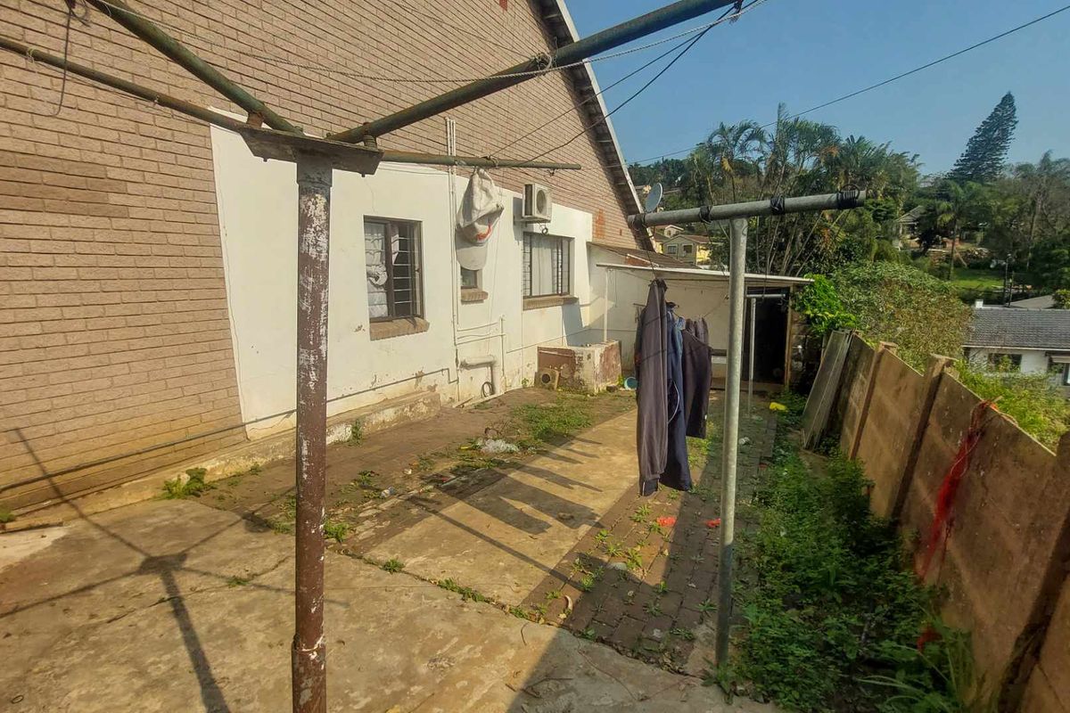 Rear exterior area featuring a paved patio, brick wall construction, and a precast boundary wall, requiring maintenance and landscaping improvements.