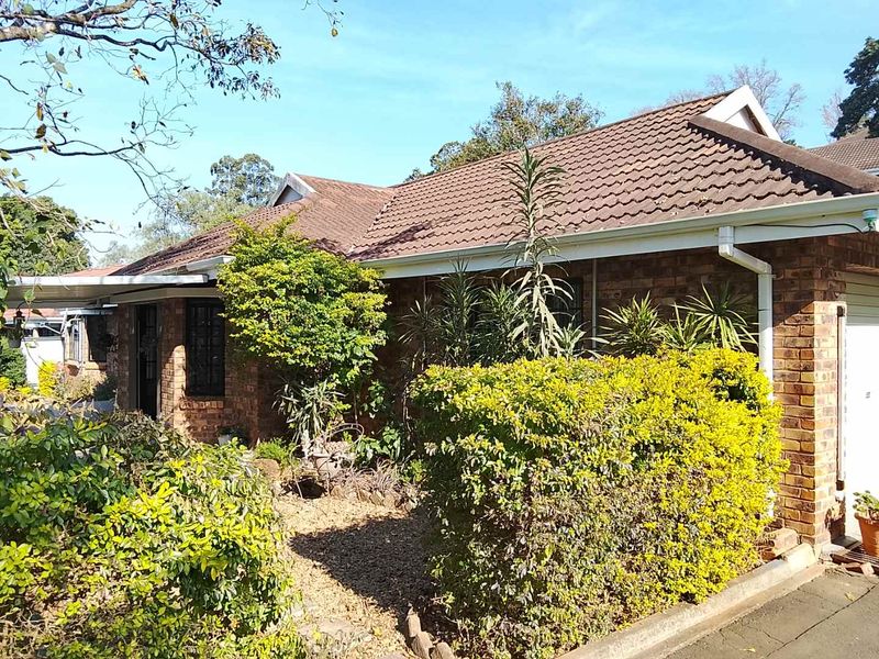 Front elevation of a face brick townhouse featuring a tiled roof, integrated garage, and established garden landscaping.