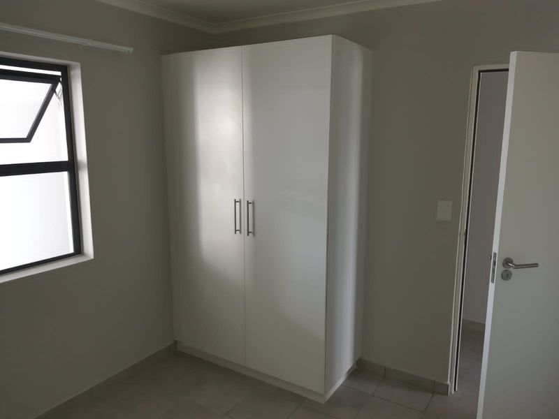 A clean, neutral bedroom featuring tiled flooring, a modern built-in wardrobe, and a casement window, offering a bright and functional living space.