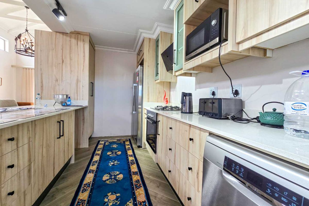 Modern galley-style kitchen featuring light wood-grain cabinetry, stone countertops, built-in oven, gas hob, and integrated microwave, offering a clean and functional workspace.