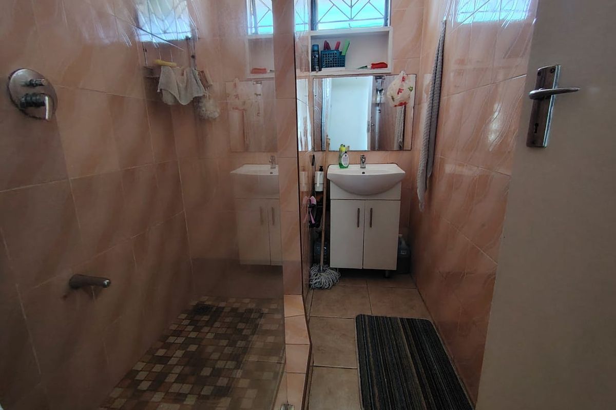 Compact bathroom featuring a shower enclosure, vanity basin with storage cabinet, and full-height wall tiling.