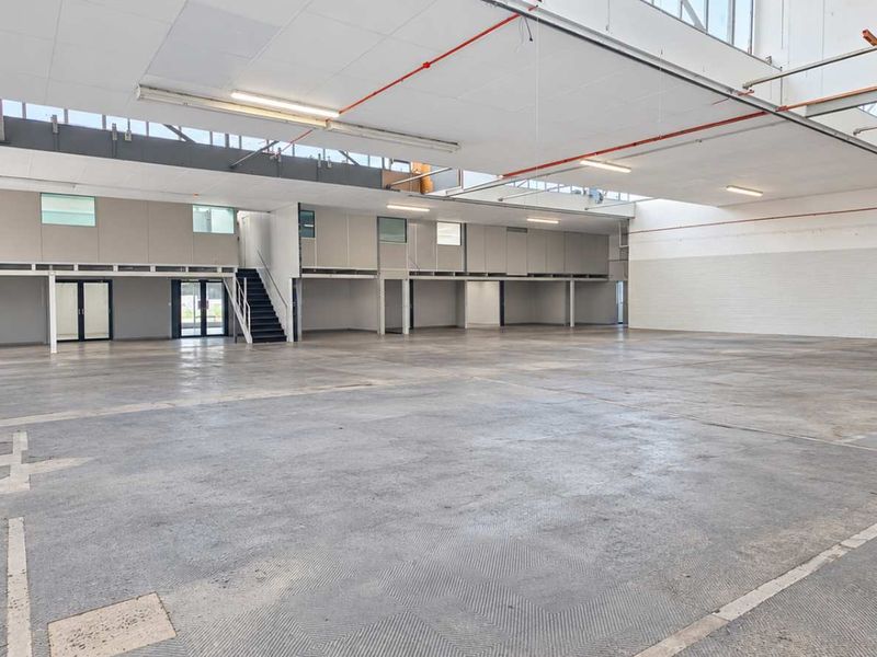 Spacious industrial open-plan warehouse featuring high ceilings, concrete flooring, a mezzanine level with staircase, and integrated fire safety systems.
