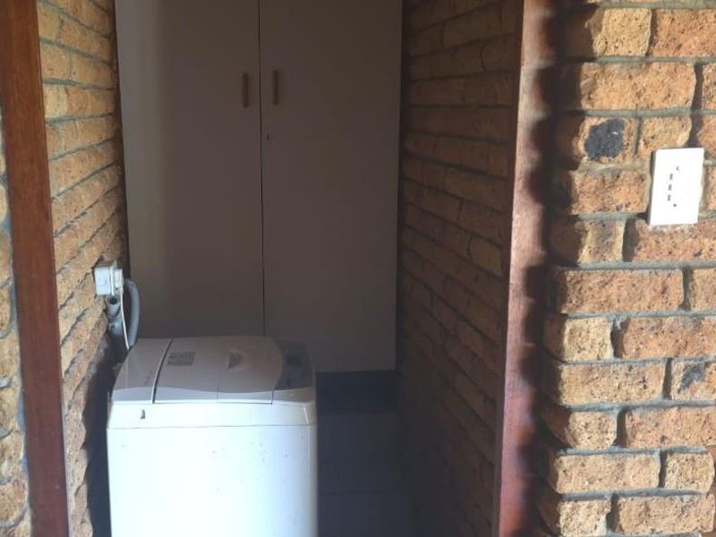 A compact laundry area featuring exposed brick walls and built-in storage cabinetry.