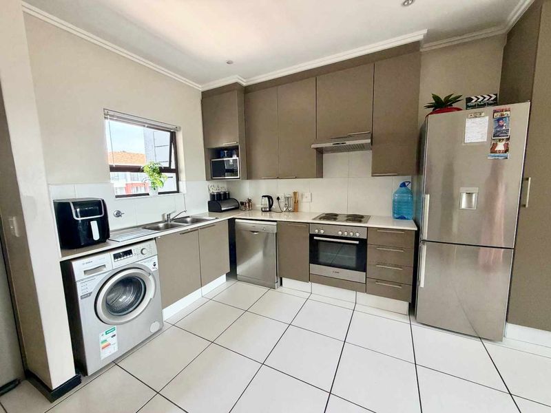 A functional kitchen featuring modern taupe cabinetry, tiled flooring, a built-in oven with hob, and integrated space for laundry and dishwashing appliances.