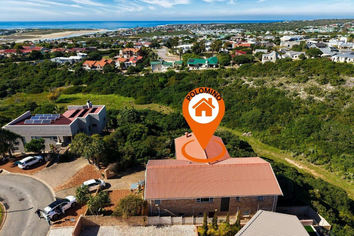 Aerial view of the property showcasing the roof structure, solar panels, paved driveway, and surrounding coastal landscape.