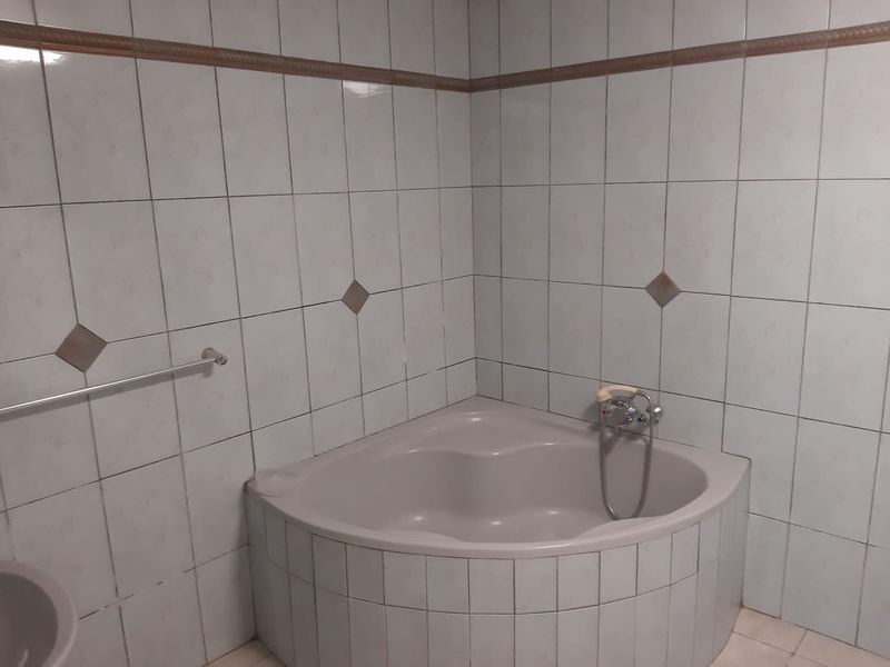 A dated bathroom featuring a corner bathtub with tiled surround and wall-mounted faucet, requiring cosmetic updates to modernize the space.